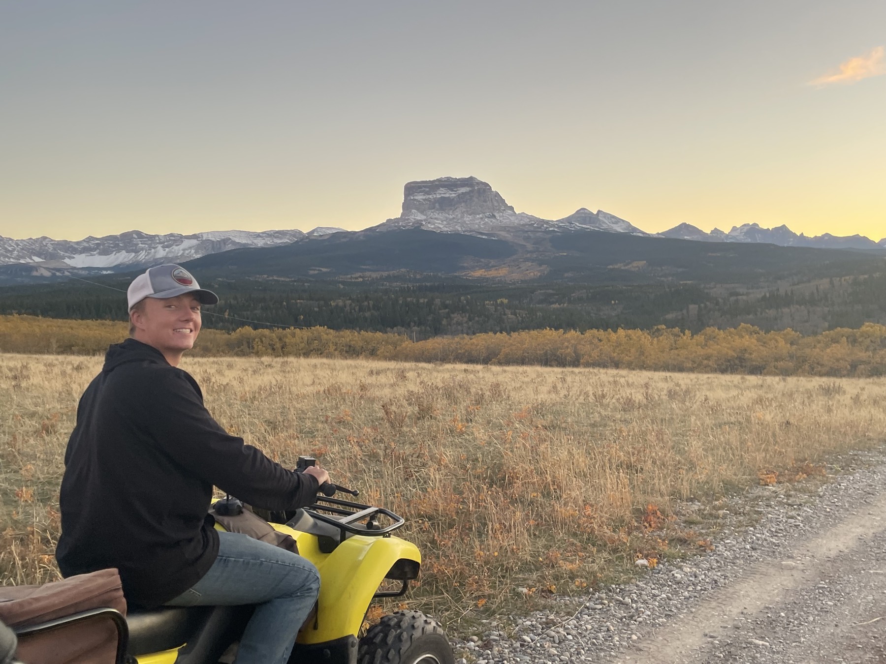 A rider on a four-wheeler looking out at Chief Mountain at sunset